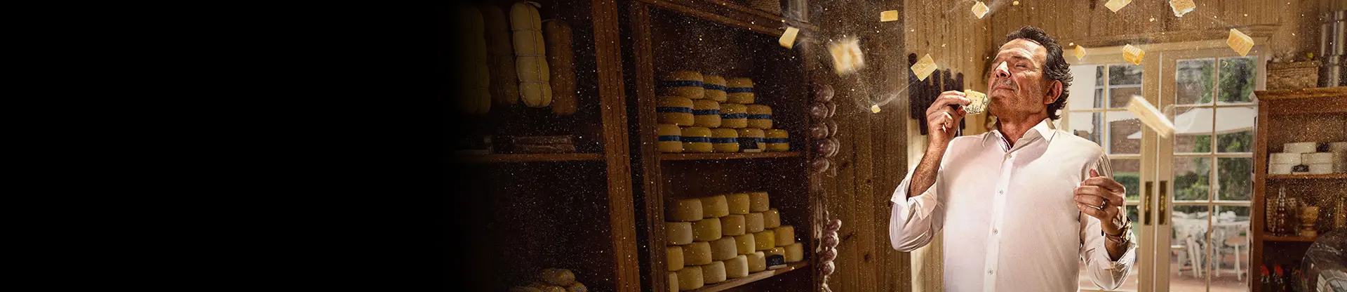 Un homme dans un magasin de fromages, entouré de fromages, sentant joyeusement un morceau avec une expression ravie.