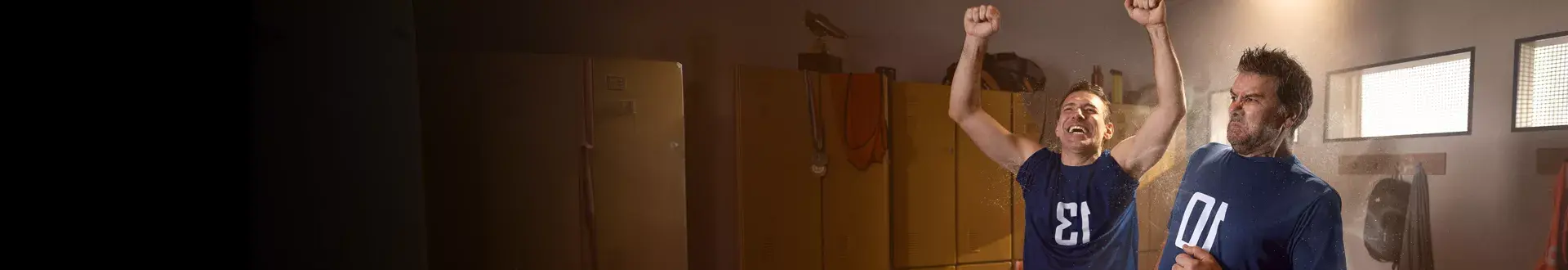 Dos hombres en un vestuario, uno celebrándolo con el brazo en alto, el otro reaccionando con asco debido al olor.
